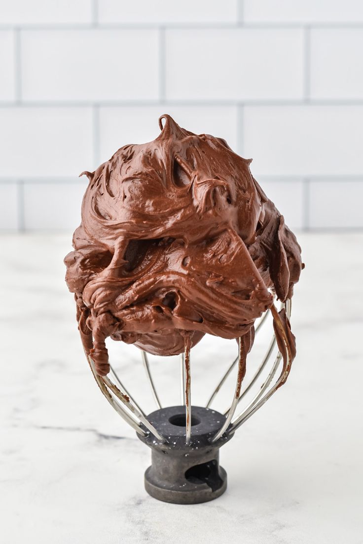 a whisk filled with chocolate frosting sitting on top of a white counter