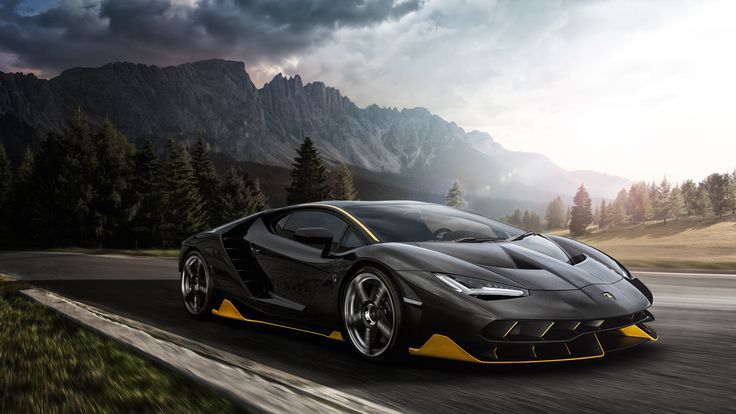 a black and yellow sports car driving down a road with mountains in the background on a cloudy day