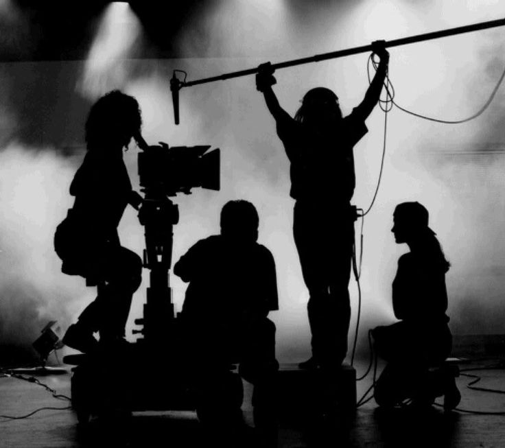 the silhouettes of people on stage are being filmed by a camera man and woman