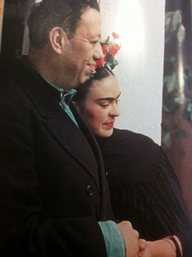 a man and woman standing next to each other in front of a wall with flowers on it