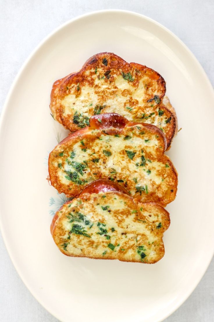 three pieces of toasted bread with cheese and toppings on a white plate next to a fork