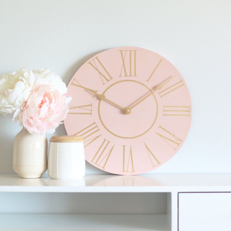 a pink clock sitting on top of a white shelf next to a vase with flowers