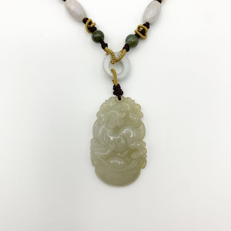 This is a high grade jadeite jade pendant necklace. It is exquisitely hand carved, so each pendant is different in some way. The pendant is completely natural jade, un-dyed and in its natural form. The pendant is carved in the form of the Chinese Zodiac - Dog. The beads above the pendant on the necklace are natural hand carved jadeite jade beads. They may not be perfectly round because they are hand carved. This gives the necklace a more rustic and natural stone like look. The years of the Dog i Engraved Jade Necklaces For Gifts, Engraved Jade Necklace For Gift, Engraved Jade Necklace Gift, Gift Engraved Jade Necklaces, Handmade Jade Necklaces For Good Luck, Traditional Engraved Jade Necklace, Spiritual Jade Medallion Necklace, Handmade Jade Necklace With Flower Pendant, Spiritual Engraved Jade Necklace