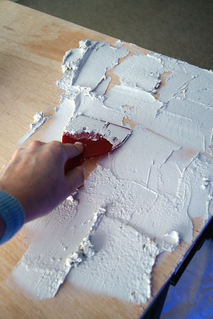 a person is using a paint brush to paint the white wallpaper on a wooden surface