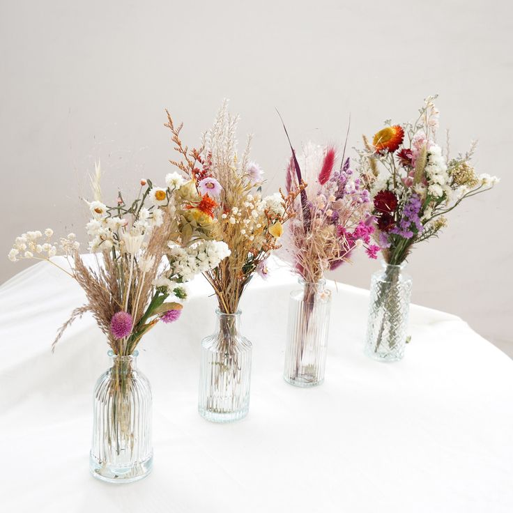 three glass vases with flowers in them on a white tablecloth covered table cloth