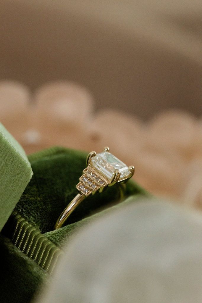 an engagement ring sitting on top of a green piece of cloth in front of a pillow