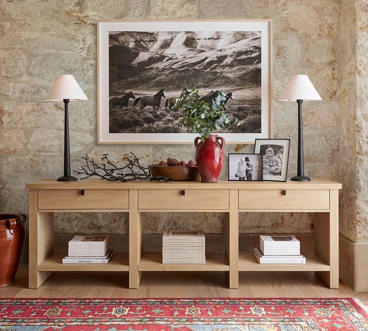 a table with two lamps and pictures on it in front of a wall mounted painting