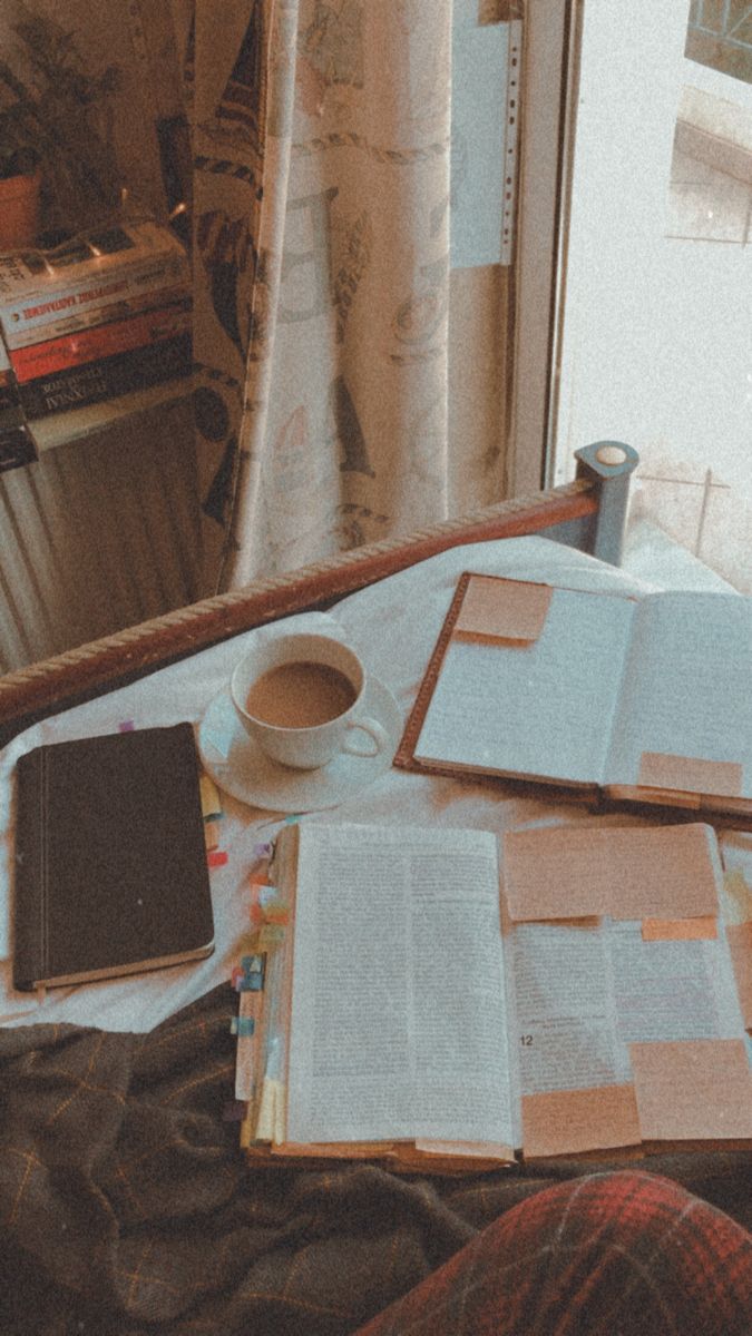 an open book and some papers on a table next to a coffee cup with a pen