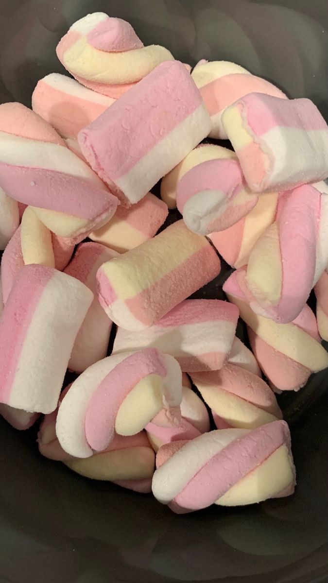 marshmallows are in a black bowl with pink and white stripes on them