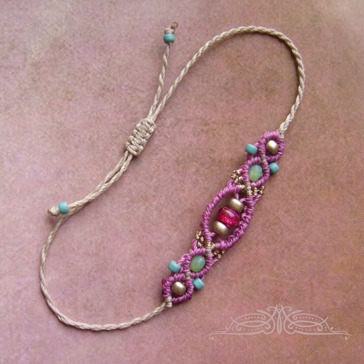 a pink and blue beaded necklace with beads on it's end, sitting on top of a purple surface