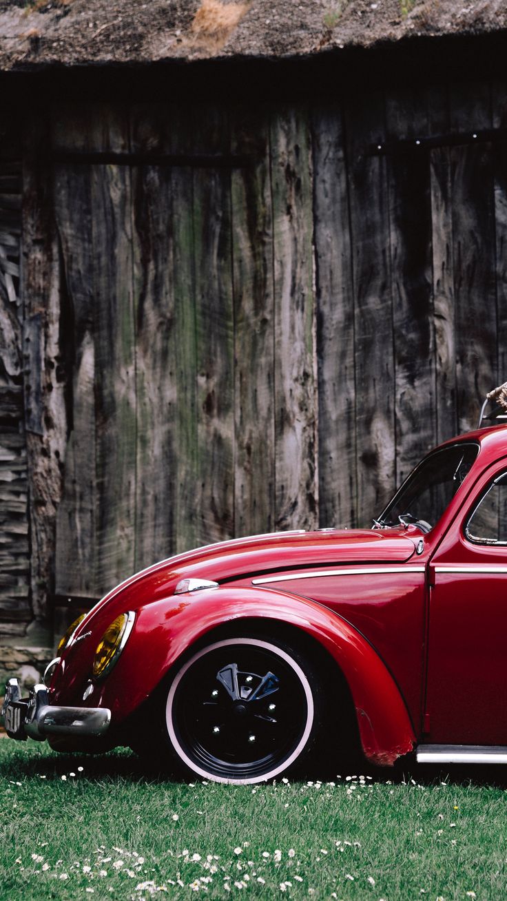 an old red car parked in front of a wooden building with a cat sitting on the roof