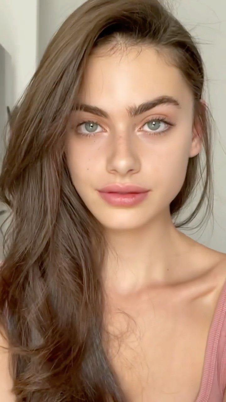 a woman with long brown hair and blue eyes is looking at the camera while wearing a pink tank top