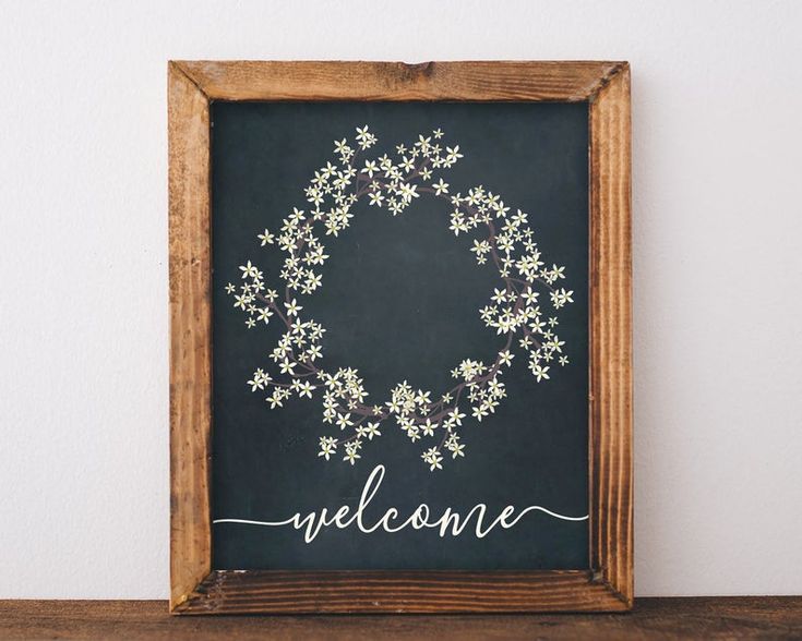 a wooden frame holding a chalkboard with the word welcome written on it and a wreath made out of small white flowers