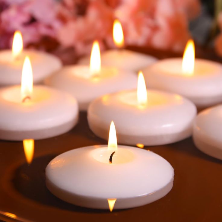 many white candles are lit on a tray with pink flowers in the backround