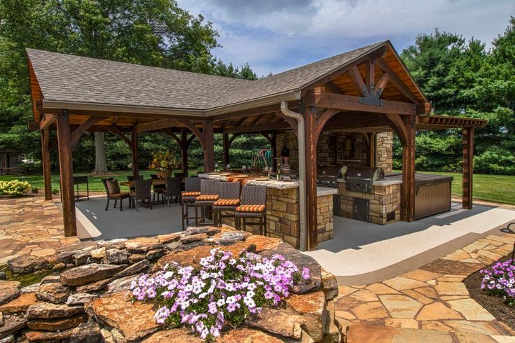 a gazebo with an outdoor kitchen and seating area in the middle of some flowers