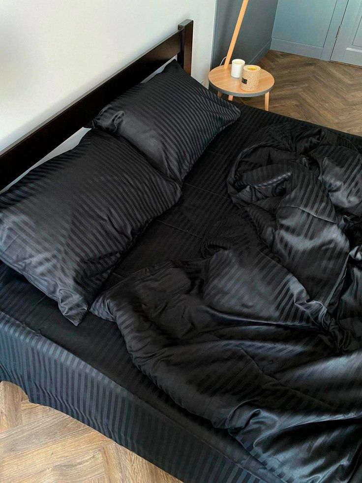 an unmade bed with black sheets and pillows on top of it in a room