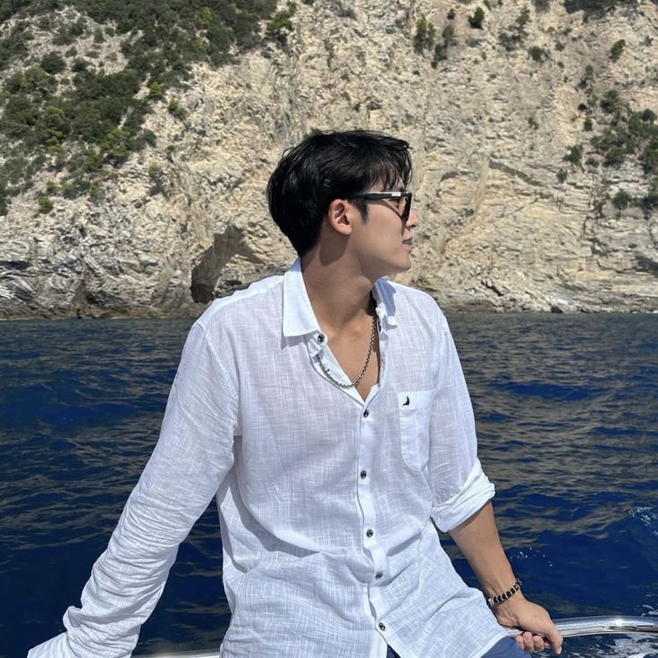 a man sitting on top of a boat in the ocean next to a rocky cliff