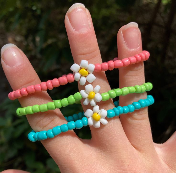 a person's hand holding three different colored beaded rings with flowers on them