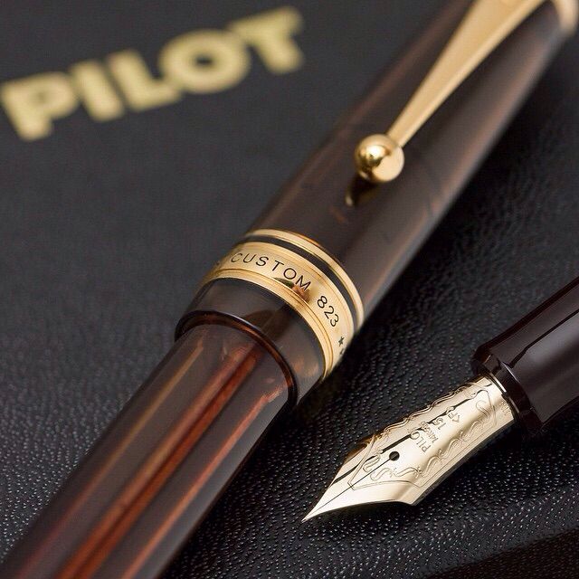 a pen sitting on top of a book next to a ballpoint pen with the word pilot written on it