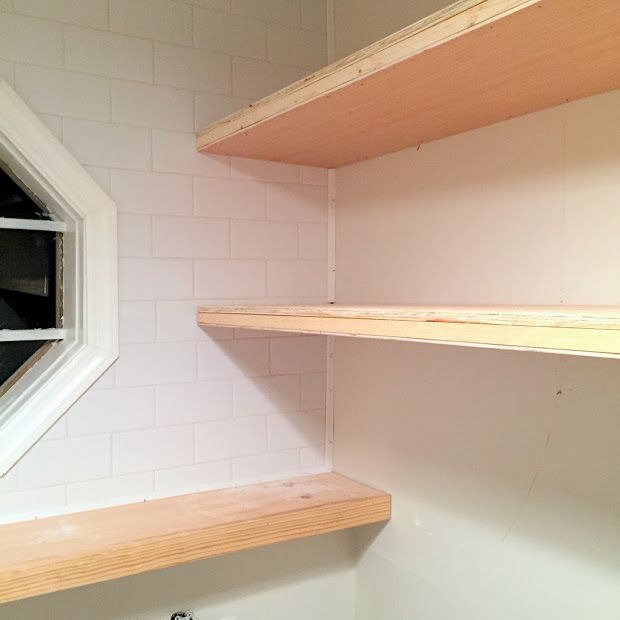 two wooden shelves in the corner of a white room with a window and sink below them