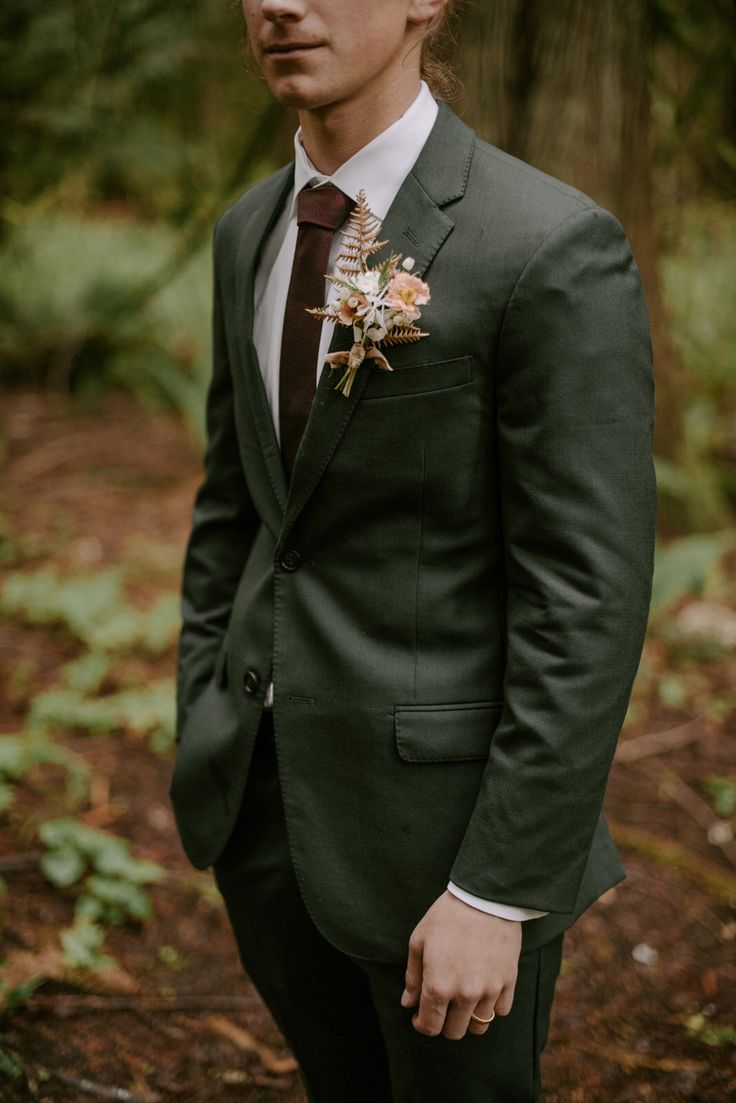 a man wearing a suit and tie standing in the woods