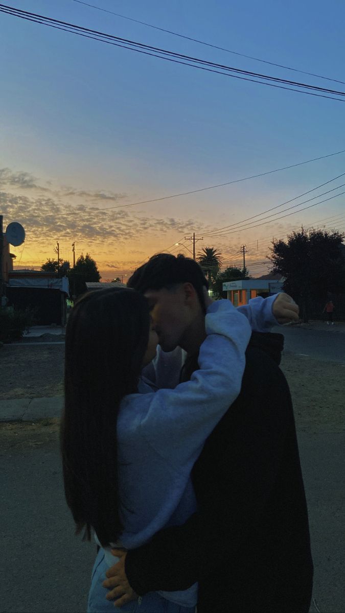 a man and woman standing in the middle of an empty street at sunset with their arms around each other