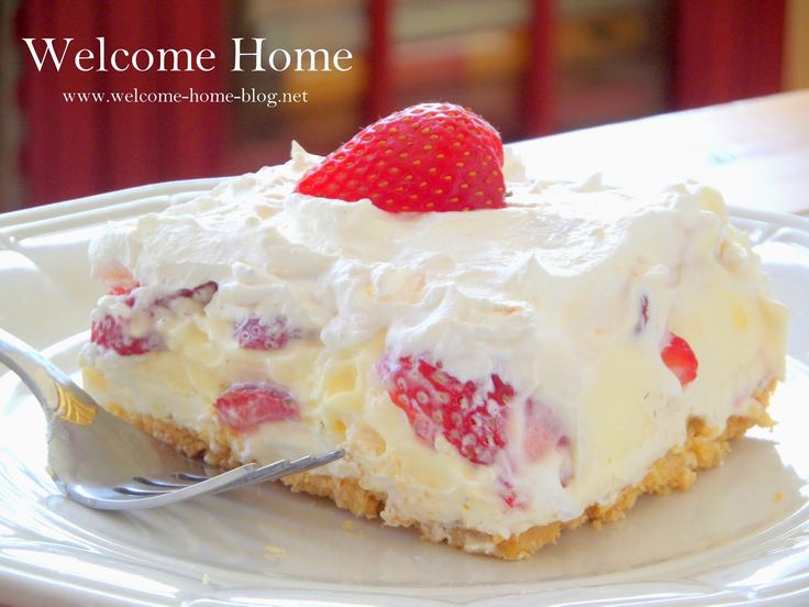 a white plate topped with a piece of cake covered in whipped cream and strawberries