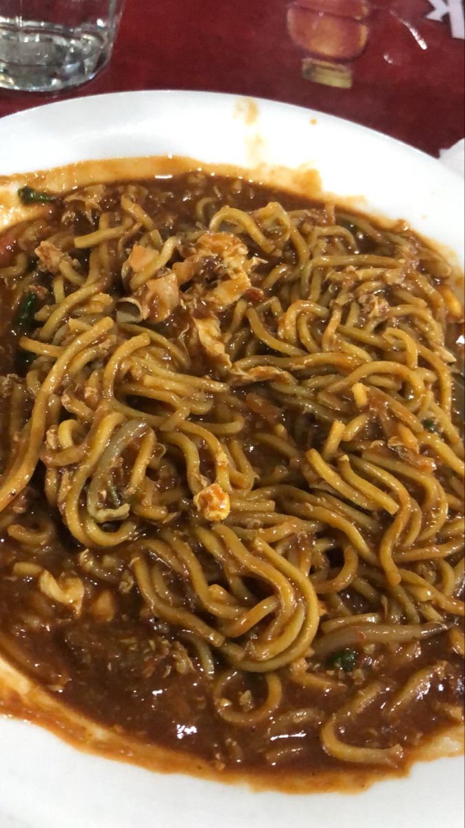 a white plate topped with noodles and sauce on top of a red cloth covered table