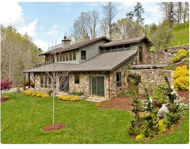 a large stone house sitting on top of a lush green hillside next to a forest