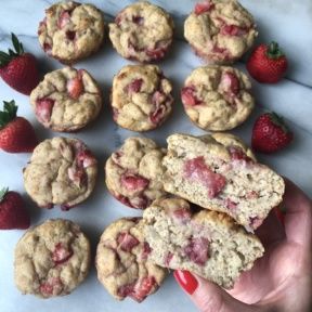 strawberry muffins and fresh strawberries on a white tablecloth with a hand holding one