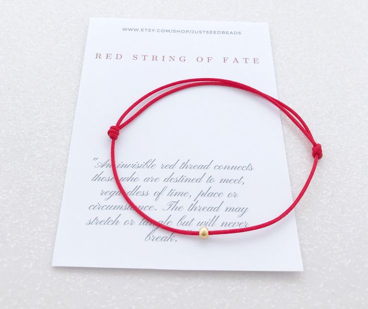 a red string bracelet with a gold bead on it, sitting on top of a card