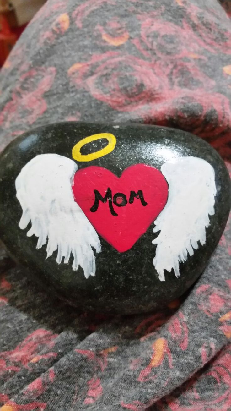 a painted rock with angel wings and an i love mom heart on it, surrounded by other rocks