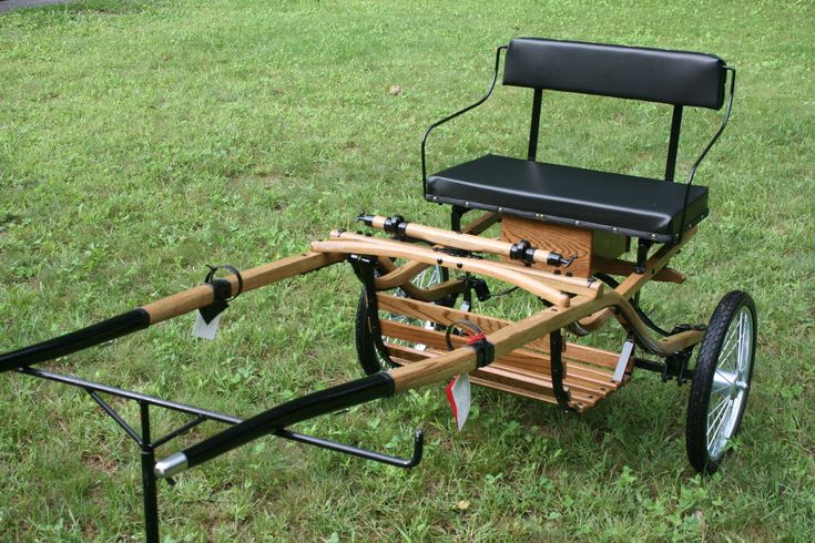 a small wooden cart with two seats on it's back wheels in the grass