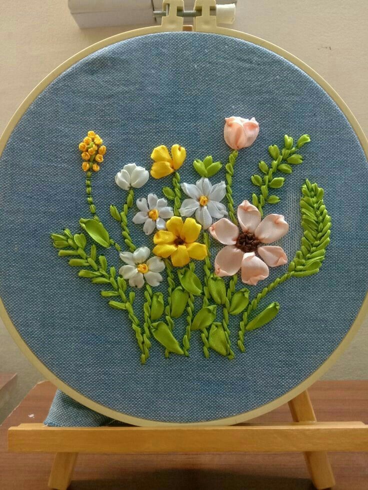 a close up of a flower embroidery on a blue surface with a wooden stand holding it