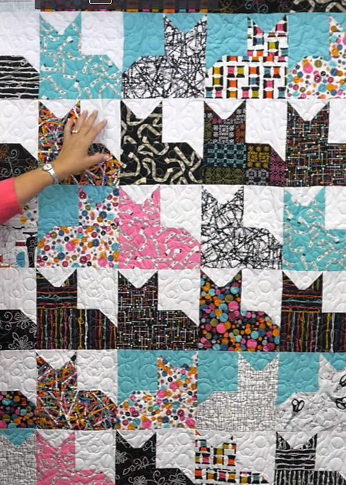 a woman is working on a quilt made with cats and kittens in black, white, pink, blue and green