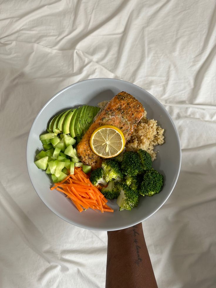 a person holding a white bowl filled with food on top of a white tablecloth