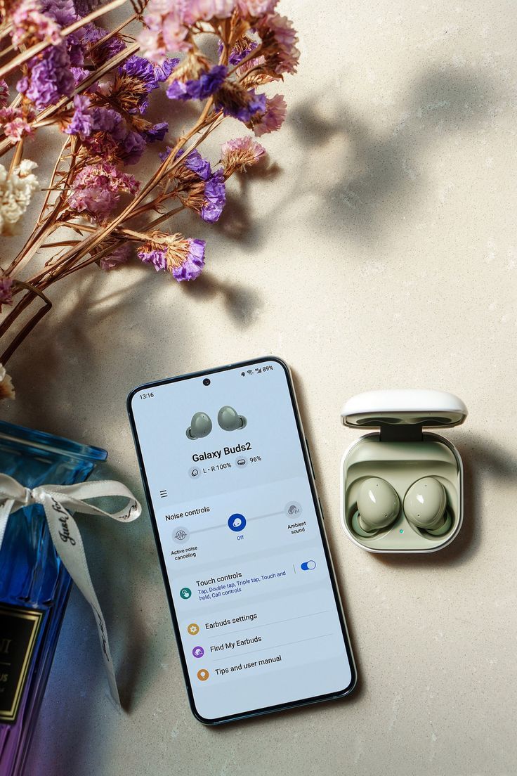 an iphone and ear buds sitting next to each other on a table with flowers in the background