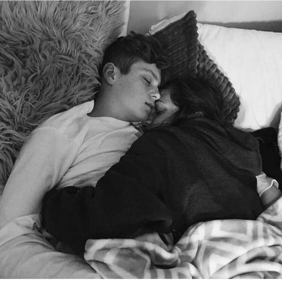 a man and woman laying in bed with blankets on top of each other, kissing