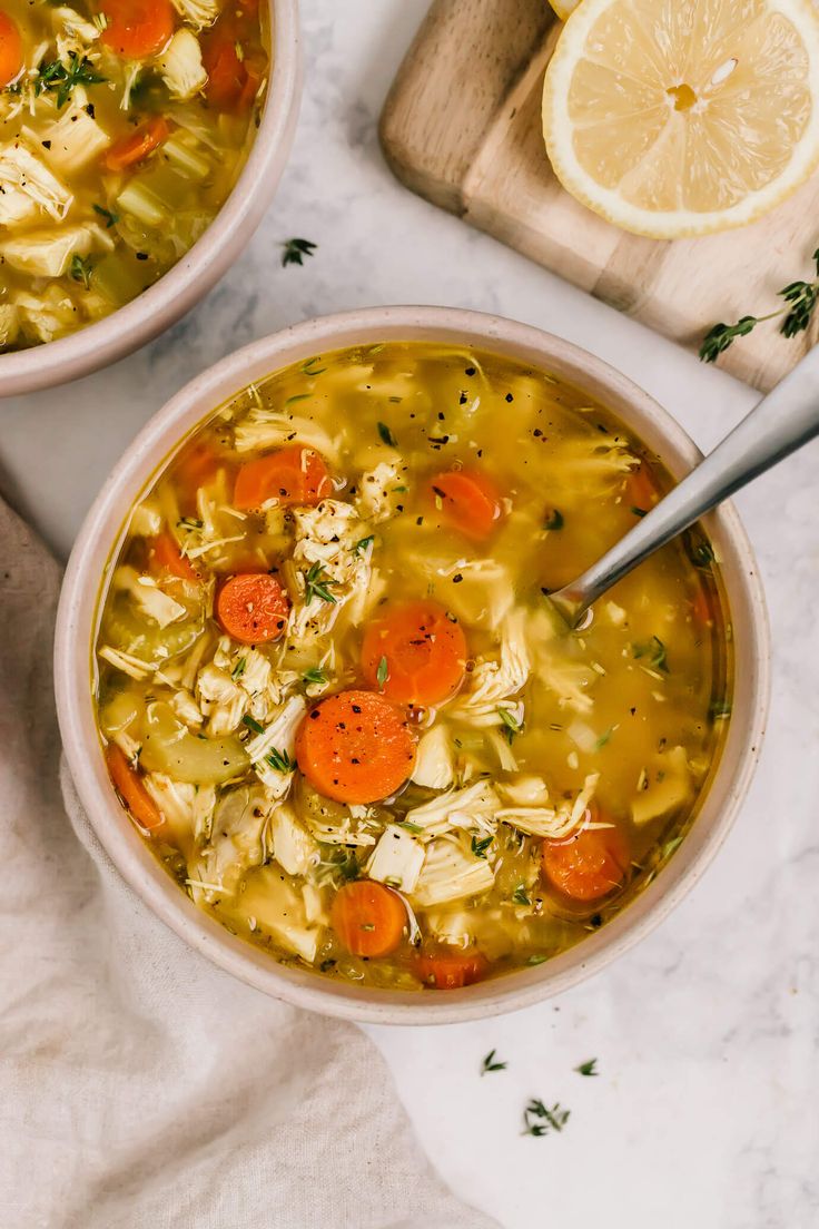 two bowls of chicken noodle soup with carrots and parsley on the side