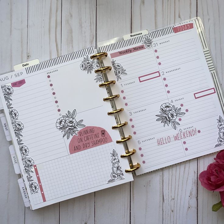 an open planner book sitting on top of a wooden table next to a pink flower