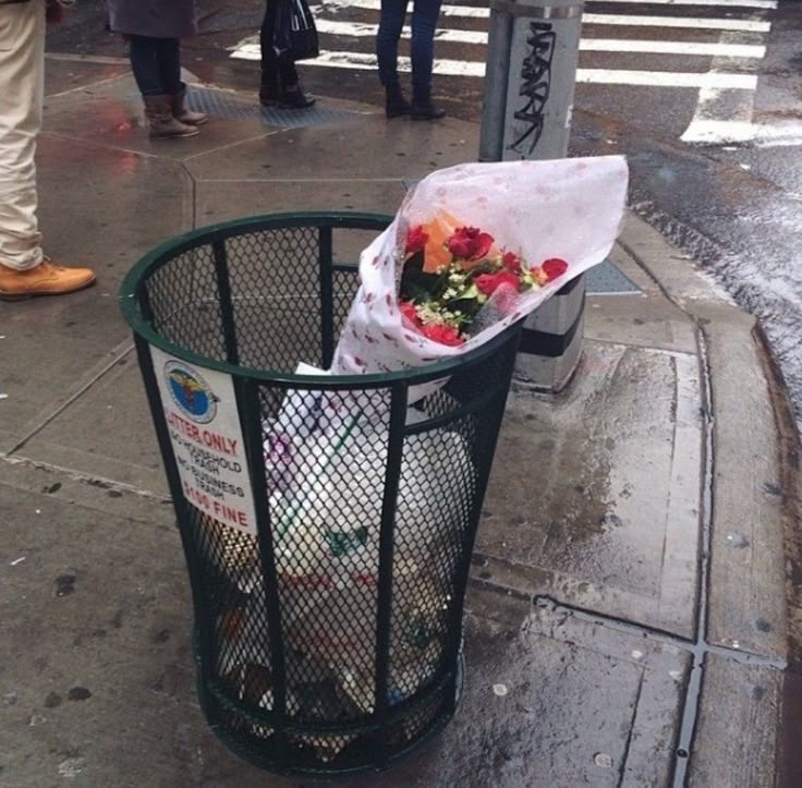 a trash can with flowers in it on the sidewalk