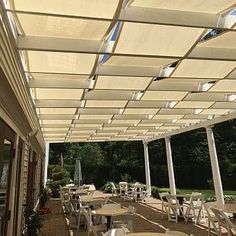 an outdoor dining area with tables and chairs under a white awning over the patio