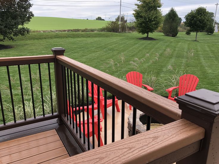 two red chairs sitting on top of a wooden deck next to a lush green field