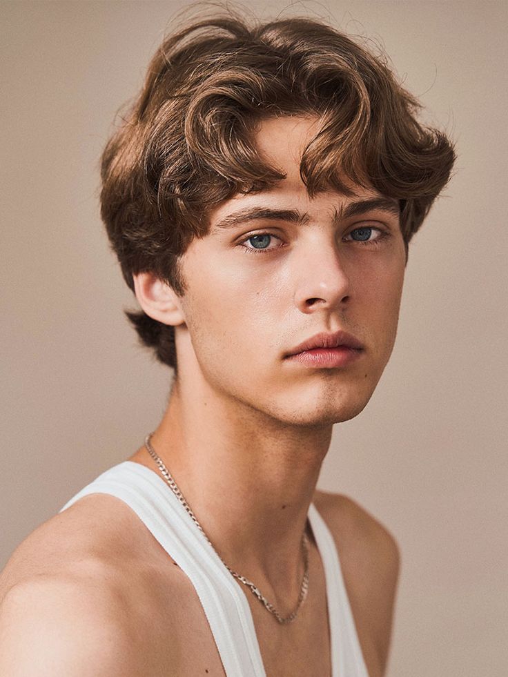 a young man wearing a white tank top looking at the camera with a serious look on his face