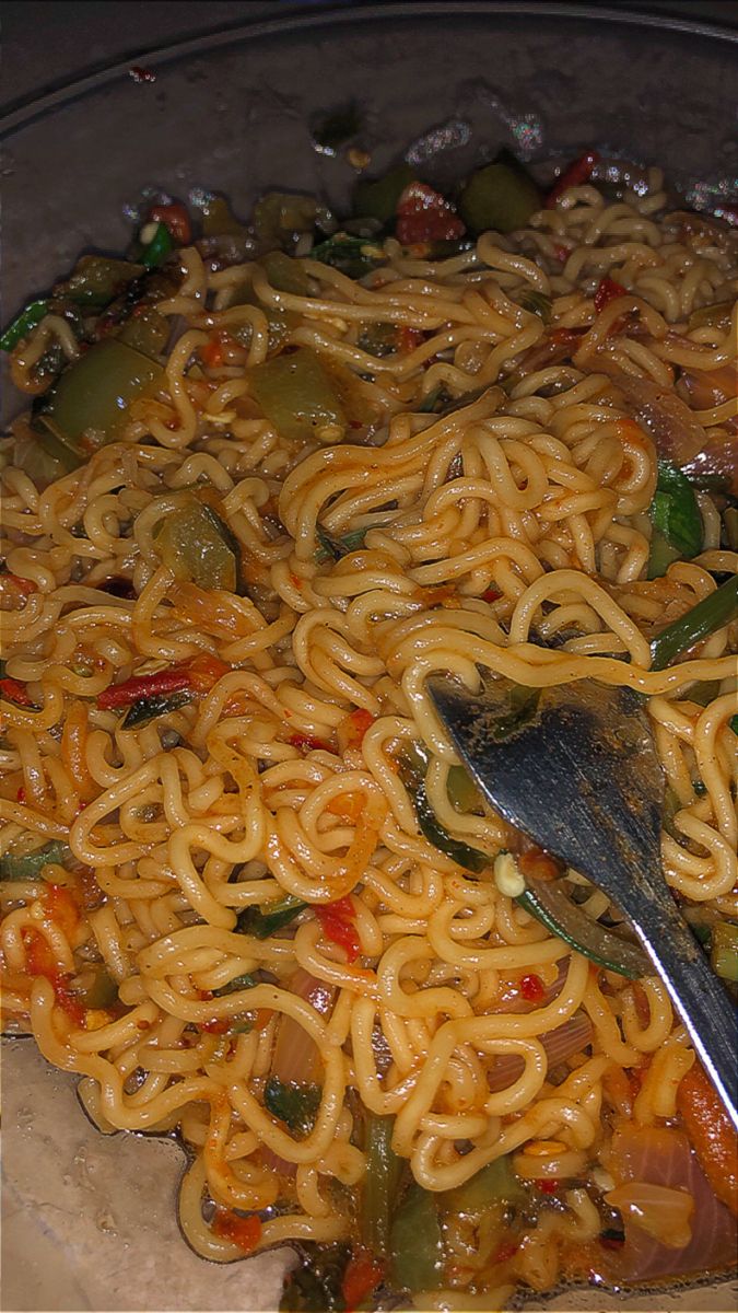 a plate full of noodles and vegetables with a fork in it, ready to be eaten