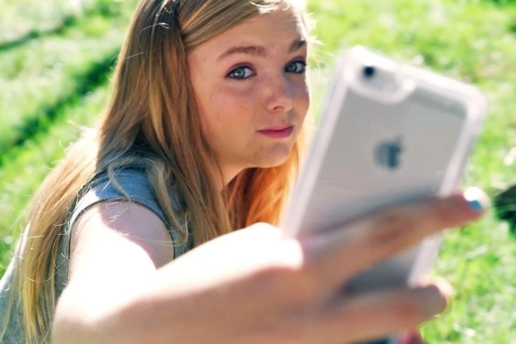 a woman sitting in the grass looking at an electronic device with her hand on it