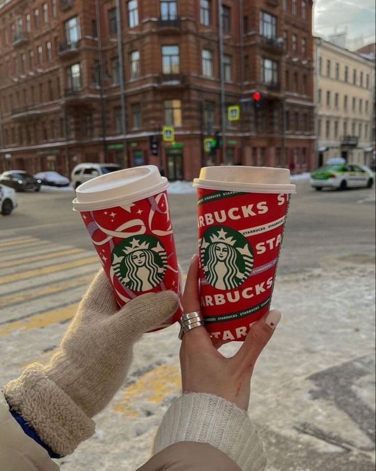 two people holding up starbucks cups in the street