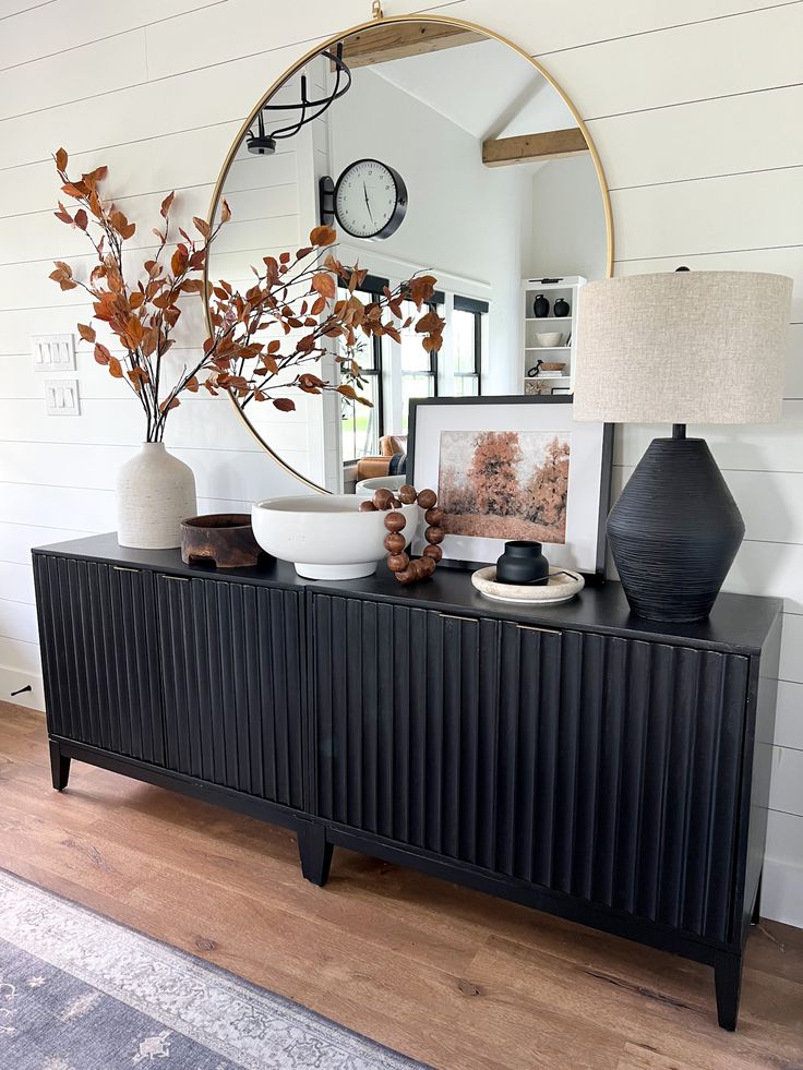 a black and white dresser with two vases on top, a mirror above it