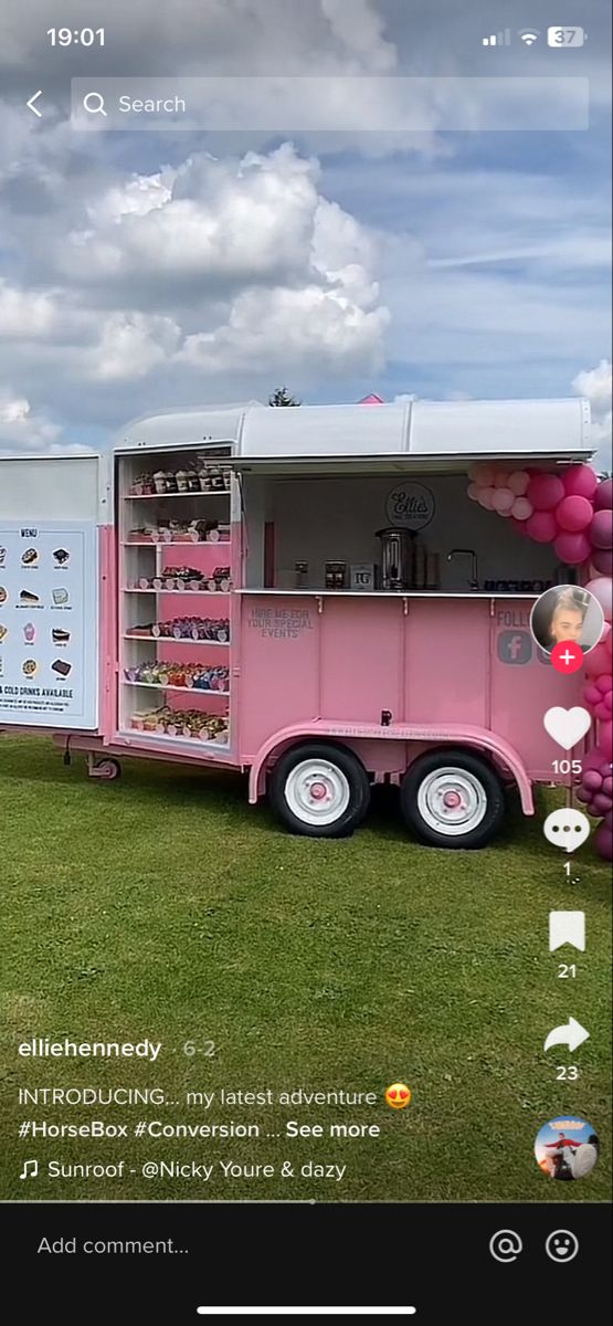 a pink food truck parked on top of a lush green field with clouds in the background