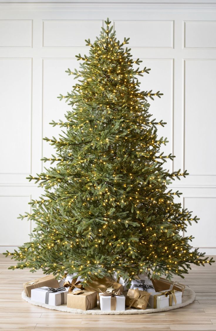 a christmas tree with presents under it on a wooden floor in front of a white wall